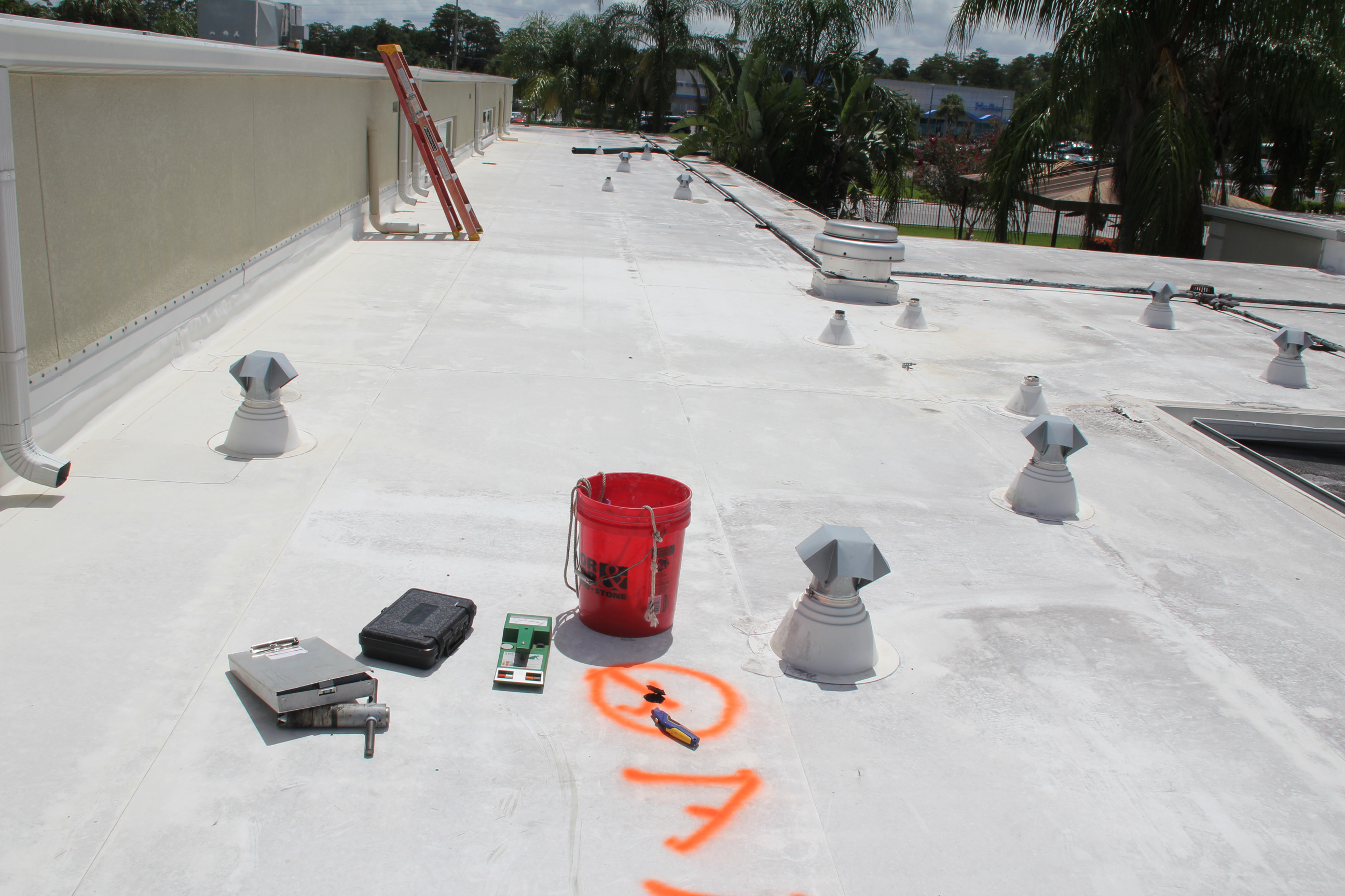 Commercial flat roof with moisture testing equipment and orange survey marks