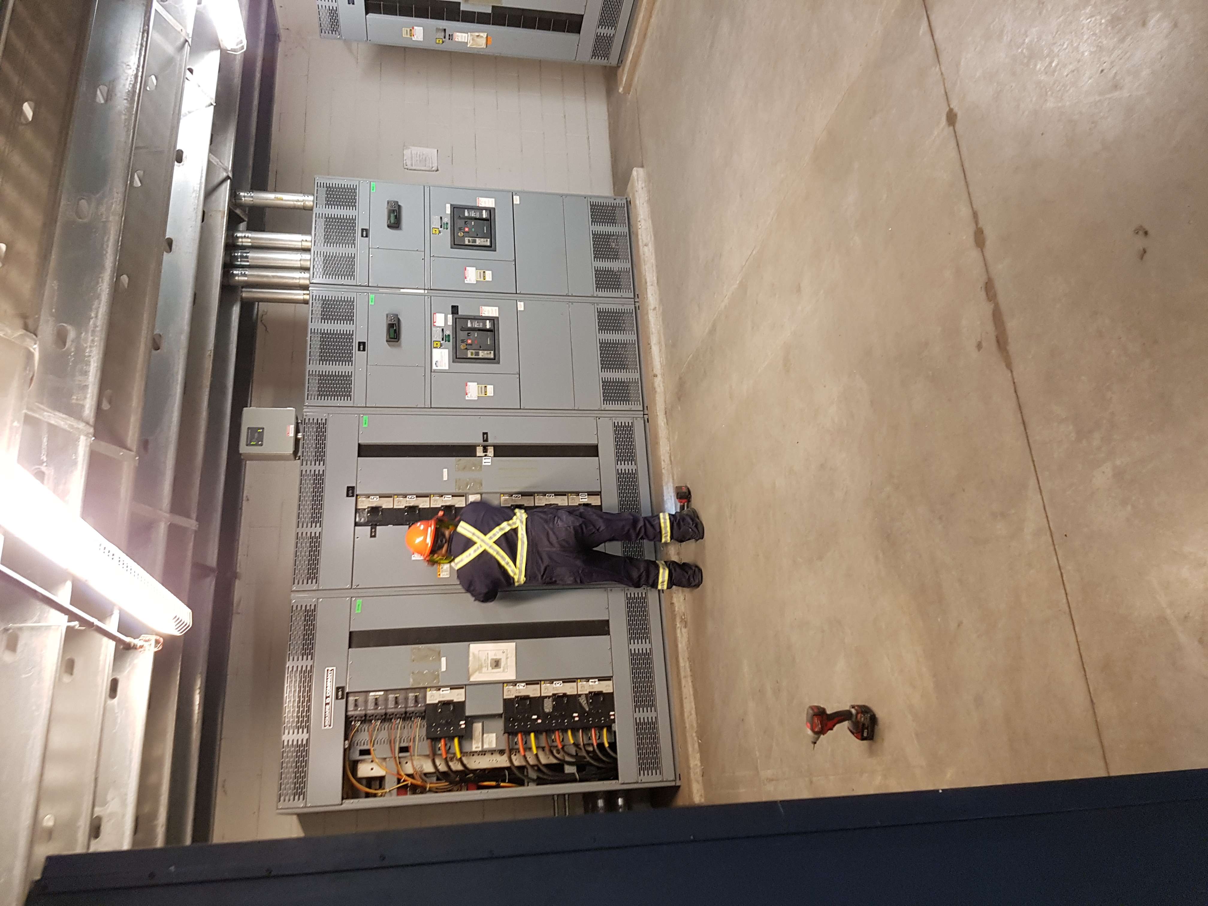 Technician in safety gear inspecting commercial switchgear in electrical room